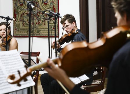 Fotografia. Koncert we wnętrzu Willi Decjusza. Muzycy grają na skrzypcach i wiolonczeli w Sali Balowej.